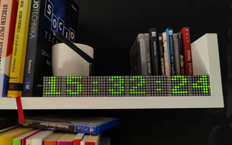 Inteligenty zegar postawiony na regale z książkami i innymi rzeczami